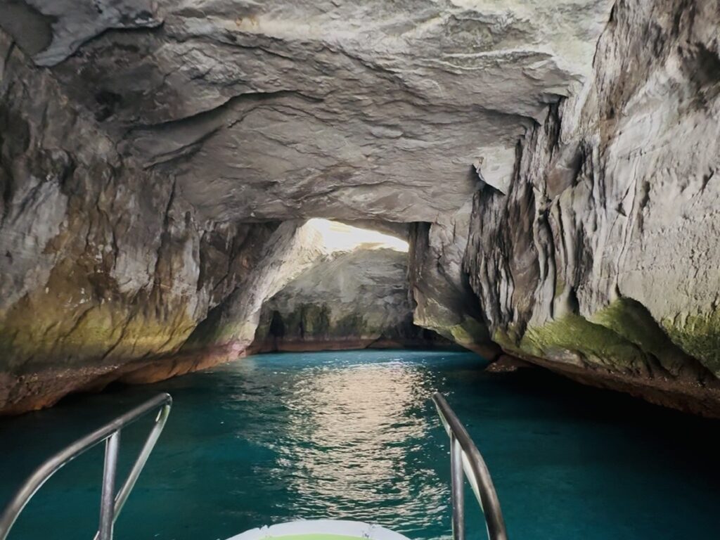 堂ヶ島遊覧船の船首から、岩に囲まれた海食洞の内部を撮影。天井の隙間から光が差し込み、エメラルドグリーンの海面を照らしている。